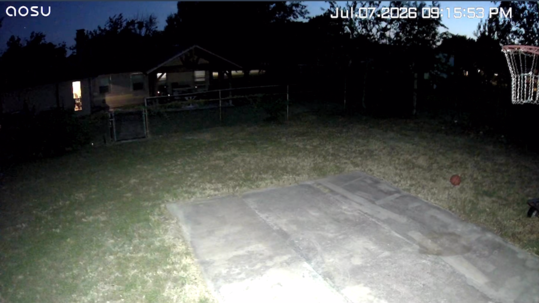 the POV of a floodlight camera lighting up a backyard at night