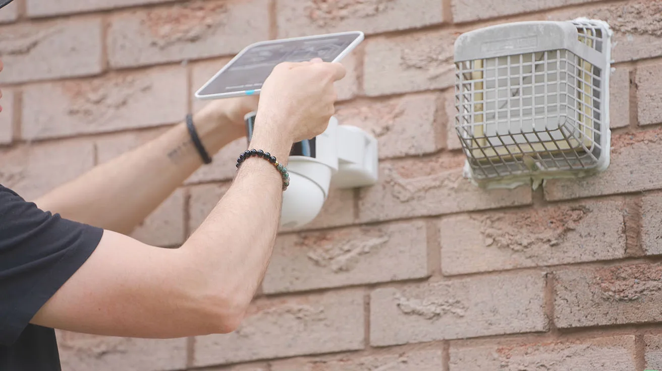 attaching security camera with integrated solar panel to base plate on brick wall