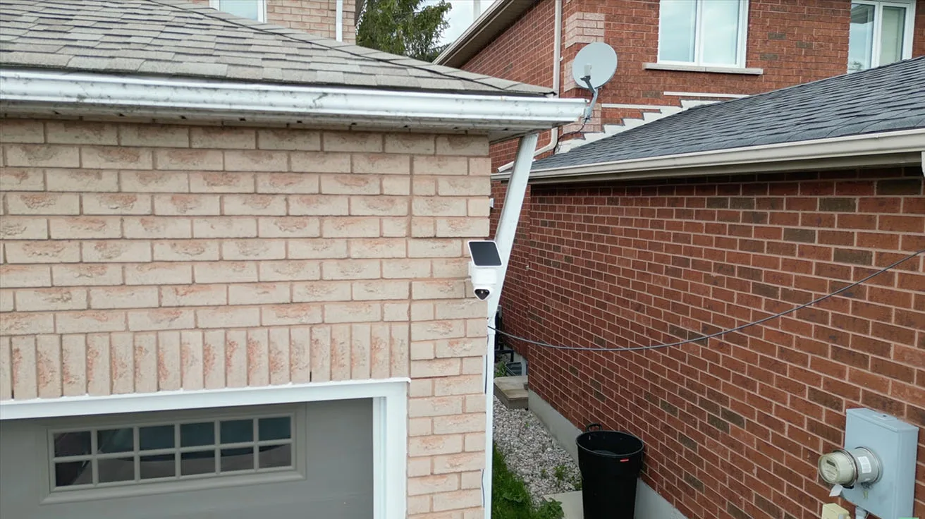 solar security camera mounted on a brick wall near a garage