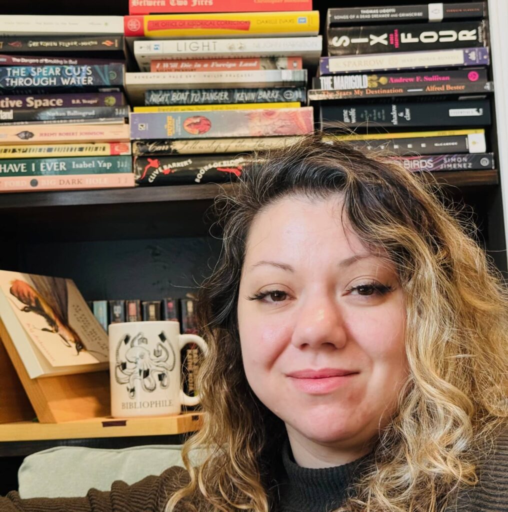 A woman with curly hair sitting in front of a bookshelf.