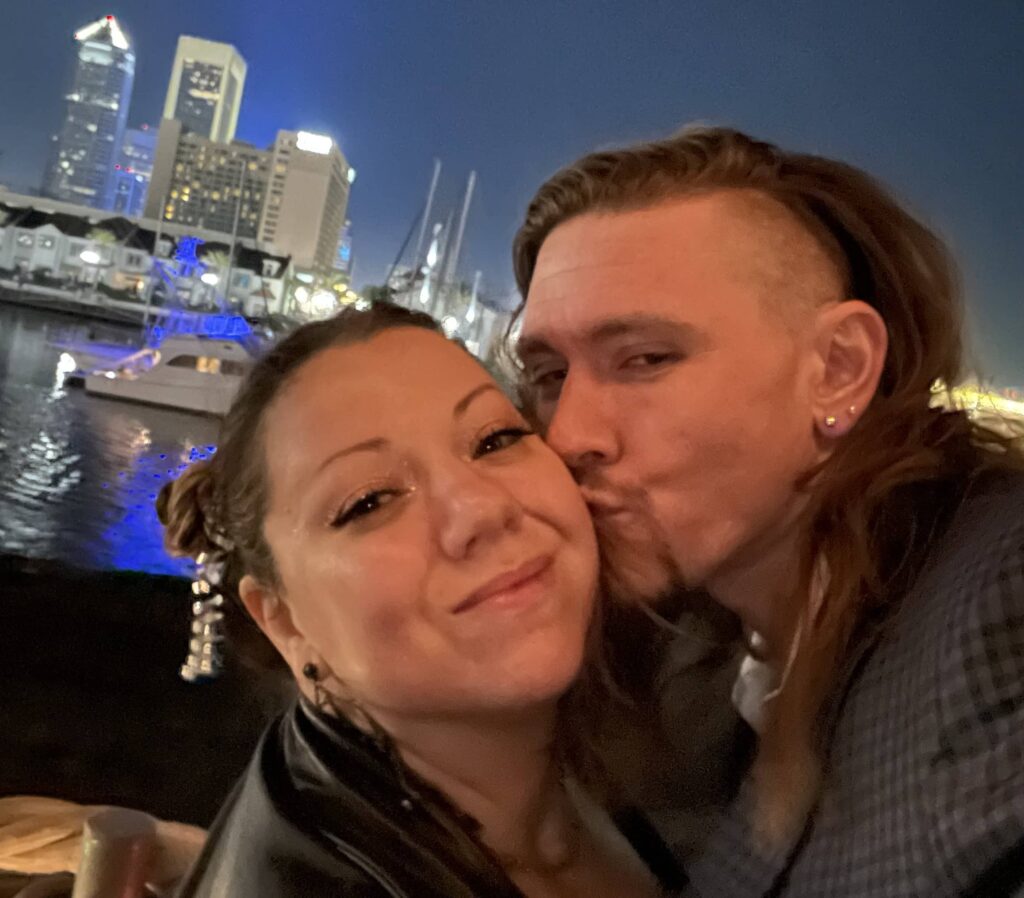A man and woman taking a selfie in front of a city skyline.