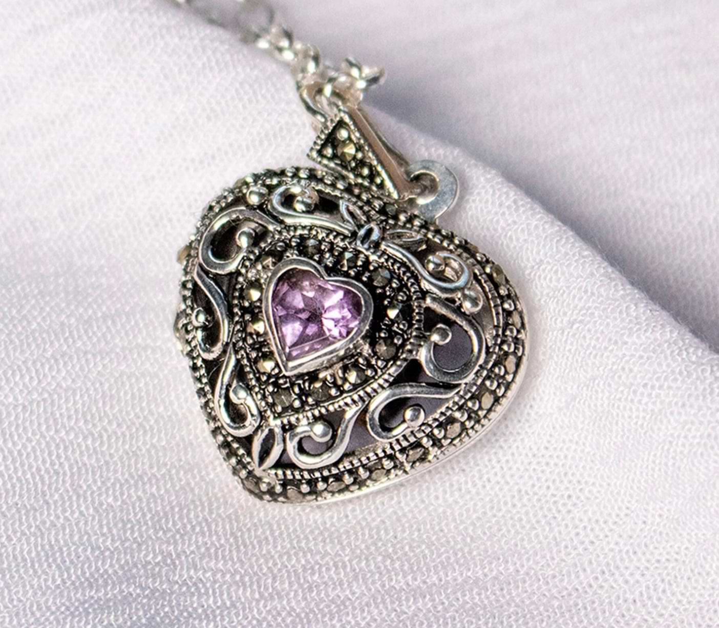 Sterling silver heart locket with amethyst centerpiece on white fabric background.