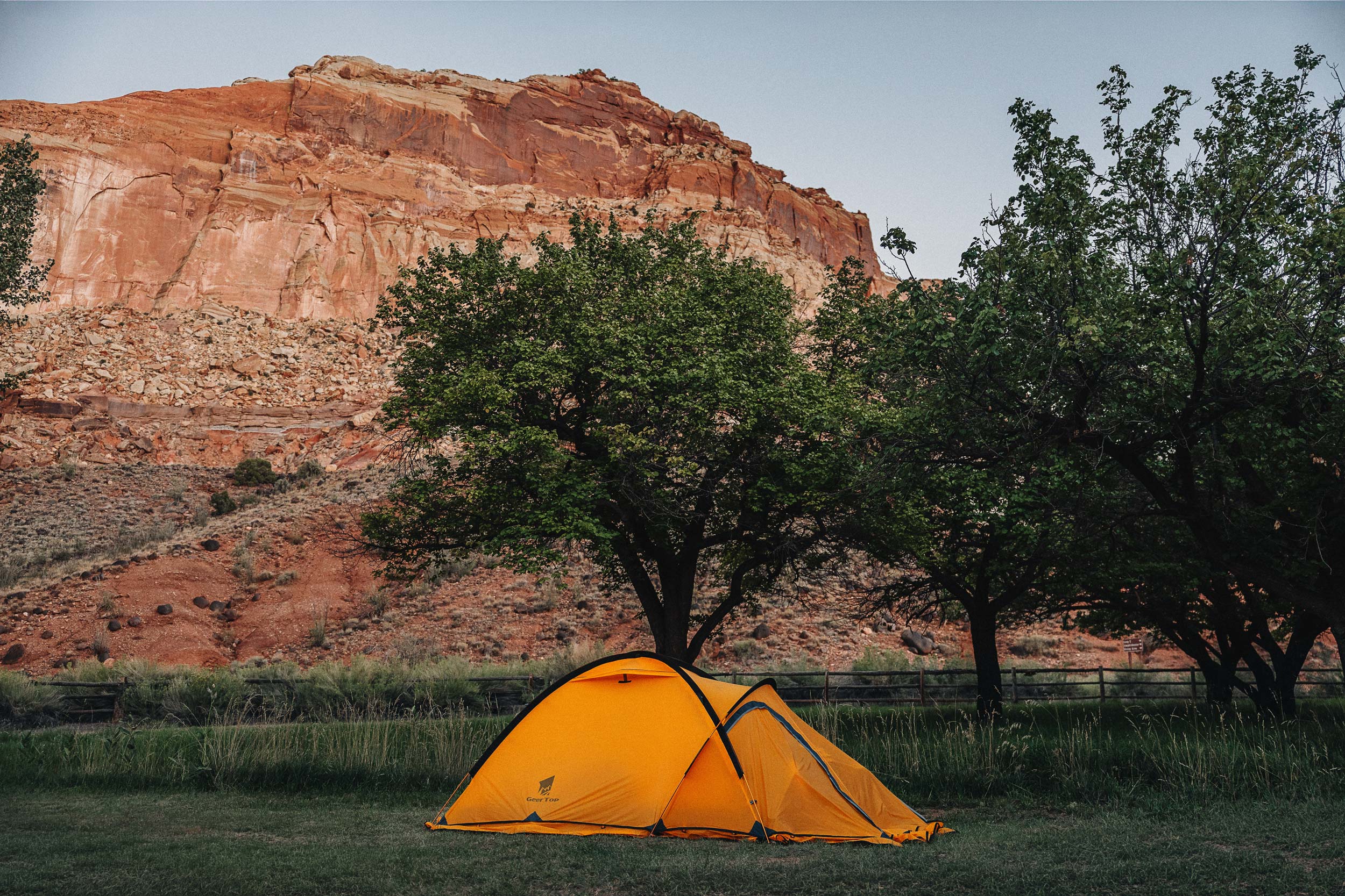 Orange motorcycle camping tent beneath red cliffs at Fruita Campground in Capitol Reef National Park.