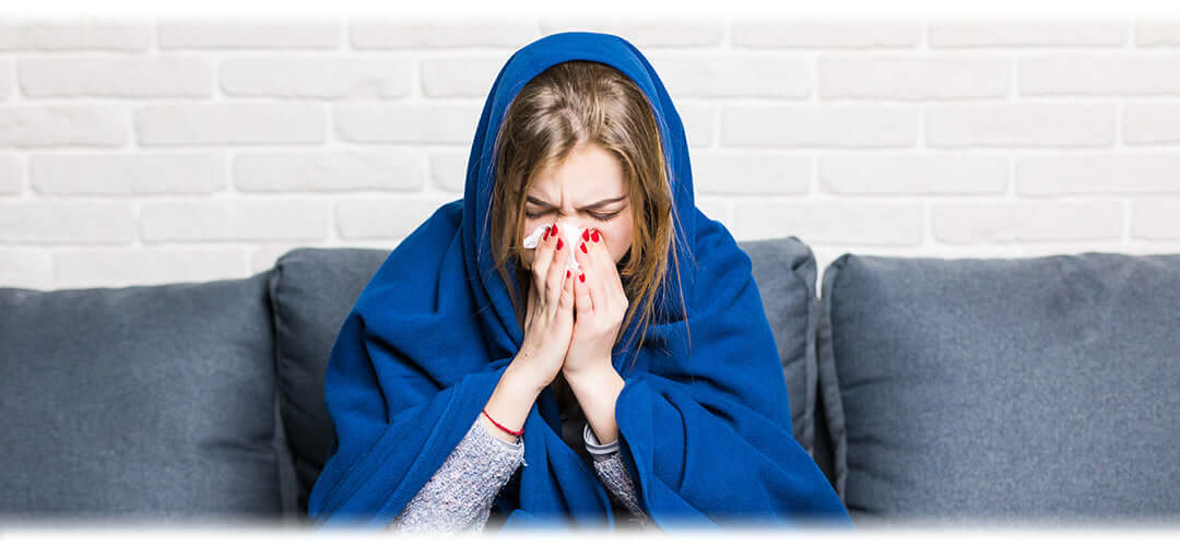 A woman wrapped in a blanket, holding a tissue, representing ways to combat the flu and seasonal illnesses