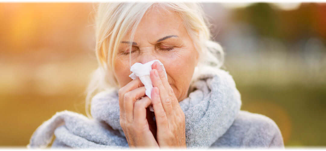 A woman blowing her nose with a tissue, indicating symptoms of a cold or allergy