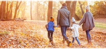 A family of four walking together through a colorful autumn forest surrounded by trees with golden and orange leaves.