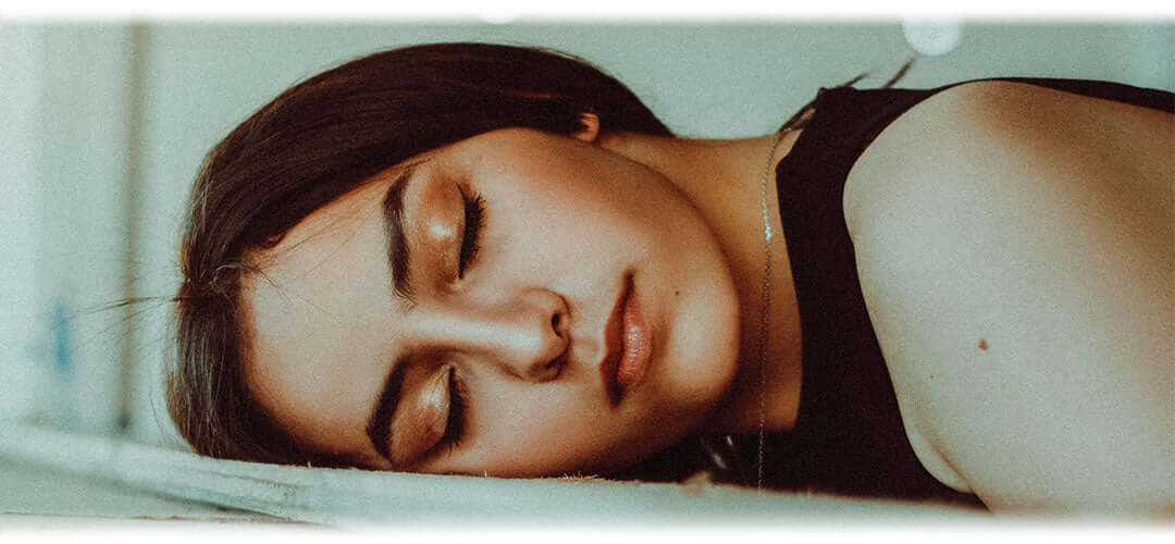 A person lying face down on a desk, appearing fatigued or exhausted