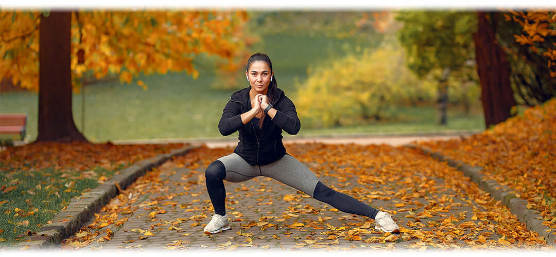 A woman stretching in a park with colourful autumn foliage, promoting outdoor fitness activities