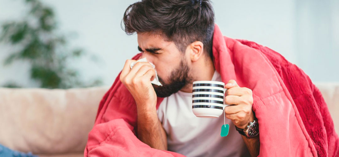 male suffering with the flue / cold wrapped up on sofa