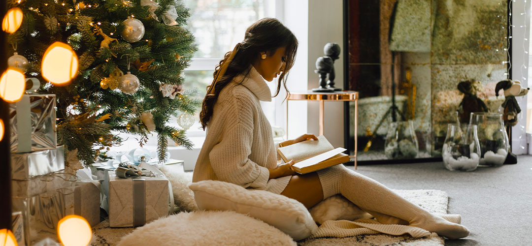 pretty-girl-sits-with-pillows-plaid-near-christmas-tree-read-book