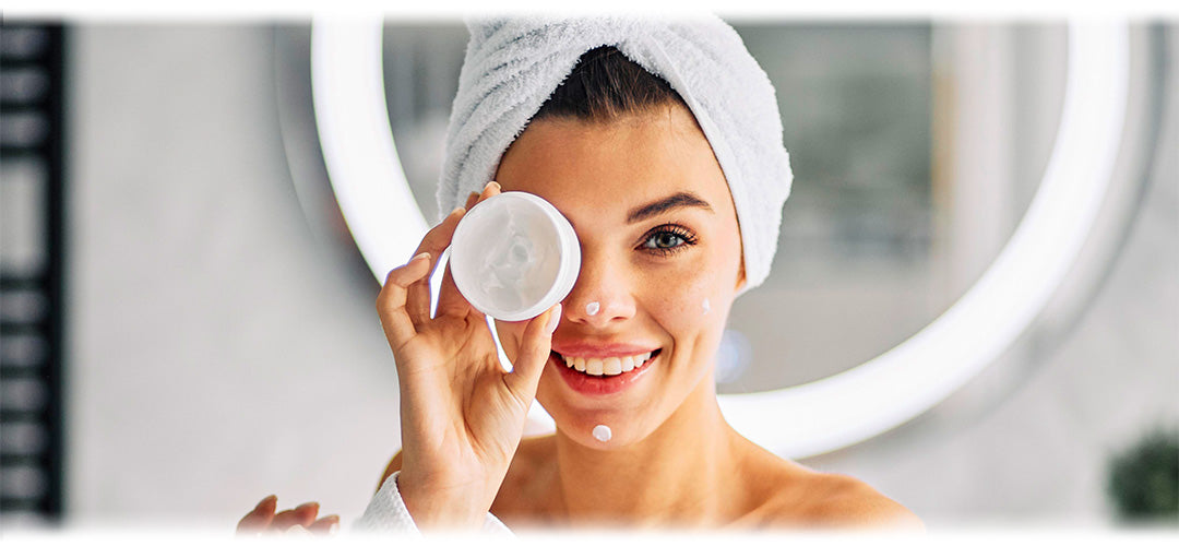 A lady wearing a towel in her hair putting moisturiser on her face