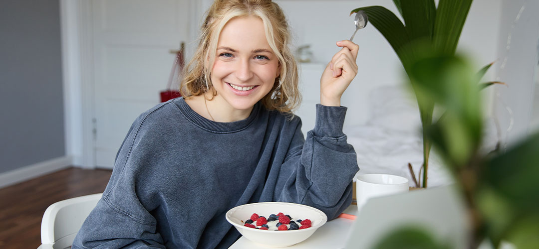 portrait-young-smiling-woman-sitting-room-watching-videos-laptop-eating-lunch-breakfast