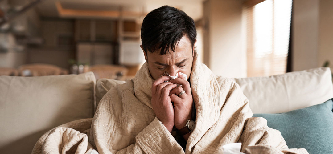 A person wrapped up in a blanket on the sofa suffering from a cold