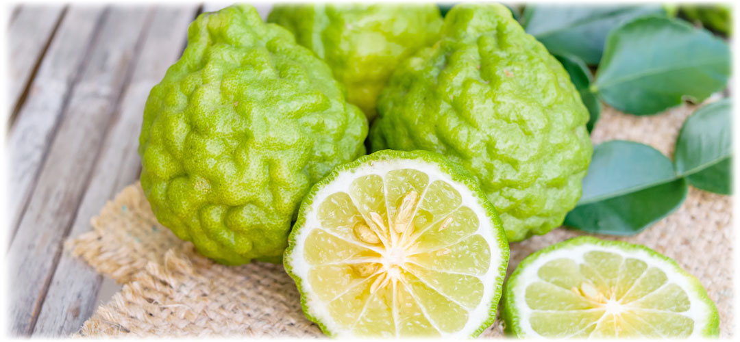 Fresh bergamot fruits, one sliced in half to reveal the vibrant green interior, placed on a rustic burlap surface next to green leaves. Represents natural health benefits and citrus freshness.