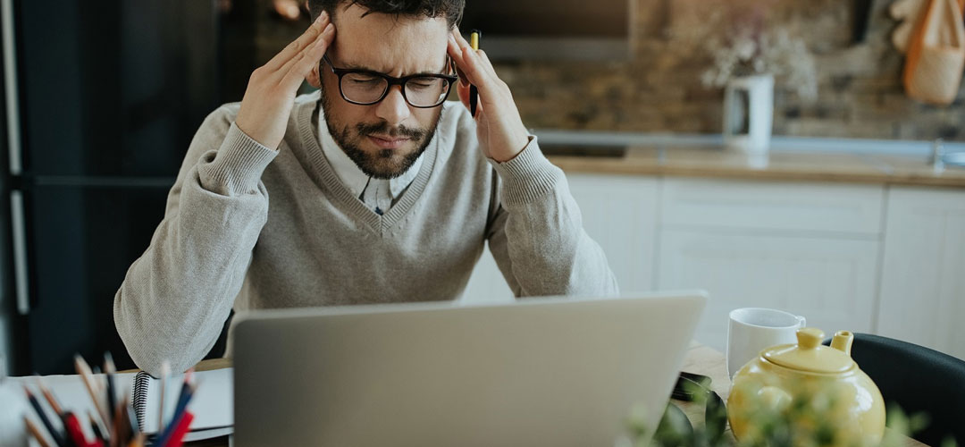 A man sat at a computer holding his head and deep breathing