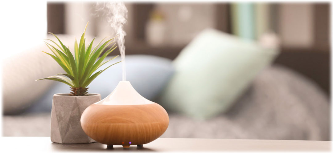 Essential oil diffuser emitting aromatic mist next to a small potted plant on a bedside table. The scene promotes relaxation and well-being.