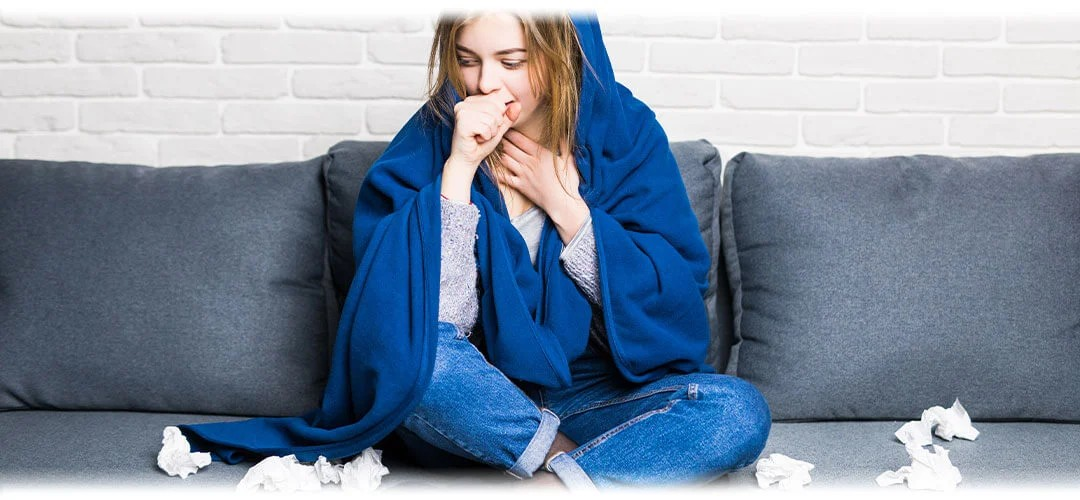 A woman suffering from a cold wrapped in a blanket surrounded by tissues