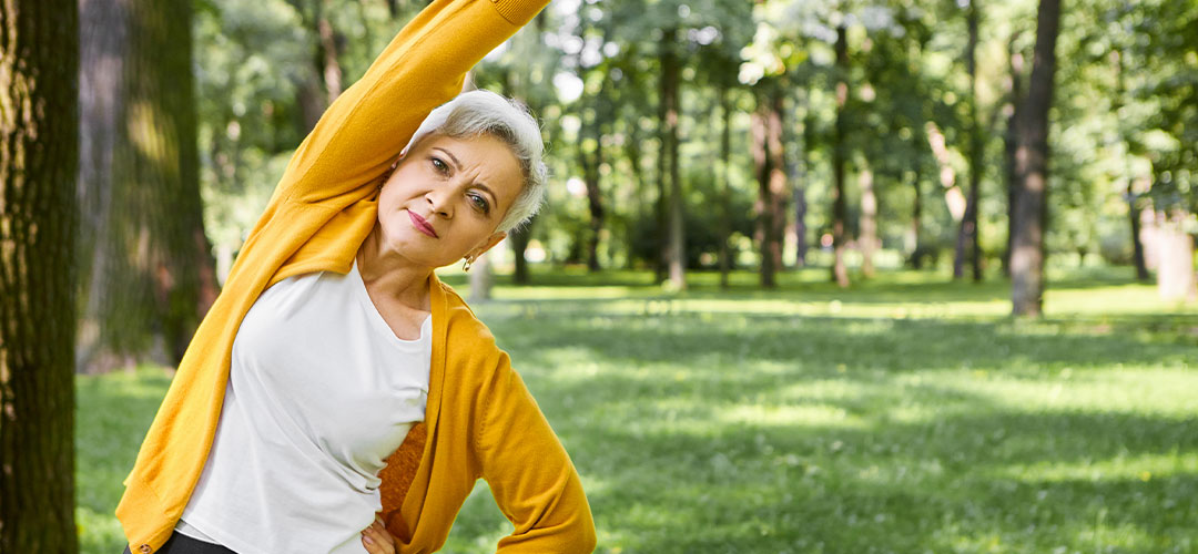 energy-health-well-being-retirement-concept-beautiful-sporty-senior-woman-with-short-hair-doing-side-bend-keeping-arm-outstretched-retired-female-exercising-outdoors-park-forest