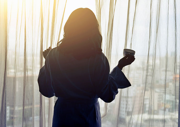 woman looking out window morning sunlight