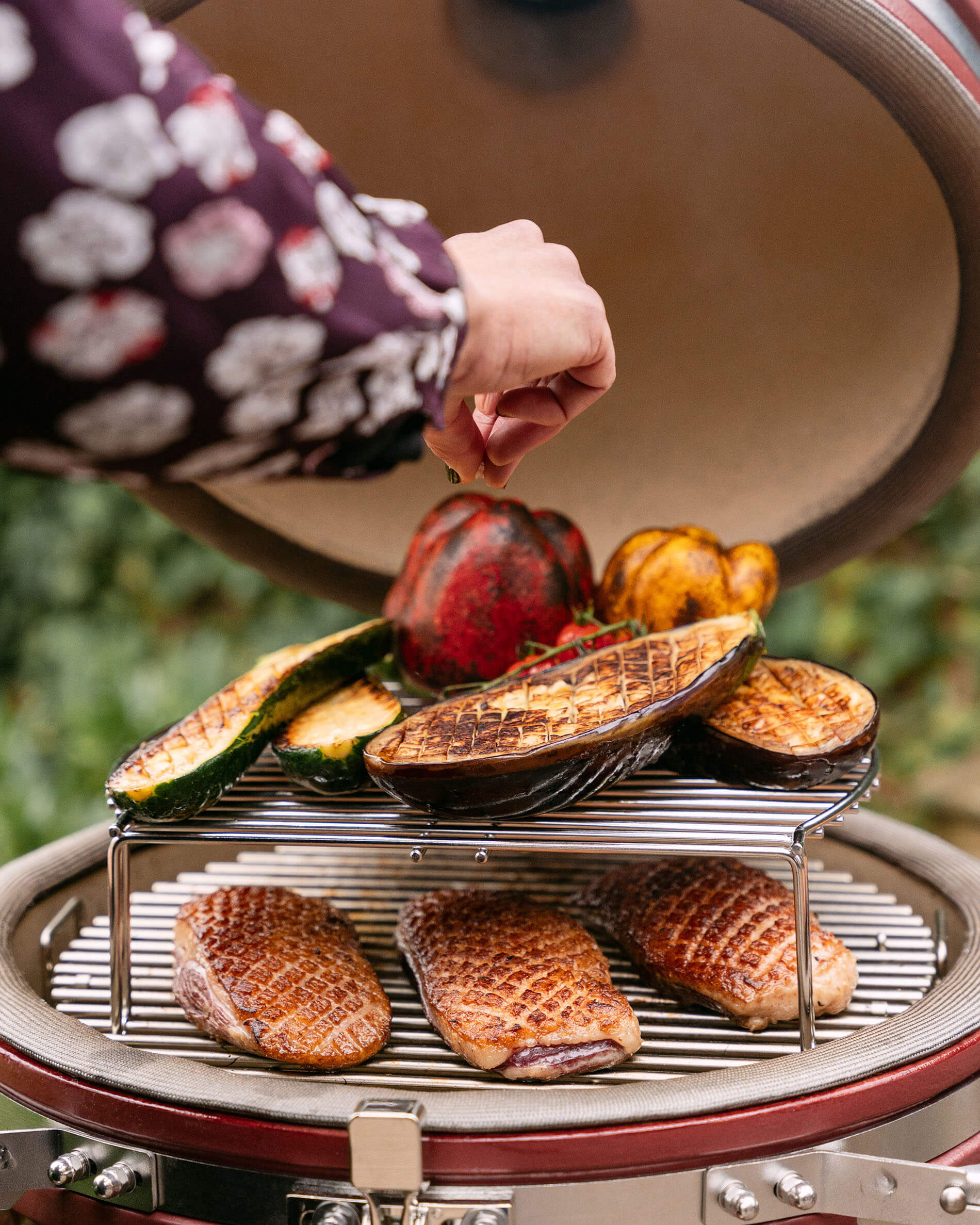 Extension de grille en inox KOKKO avec aubergines grillées et morceaux de viande en cuisson sur kamado.