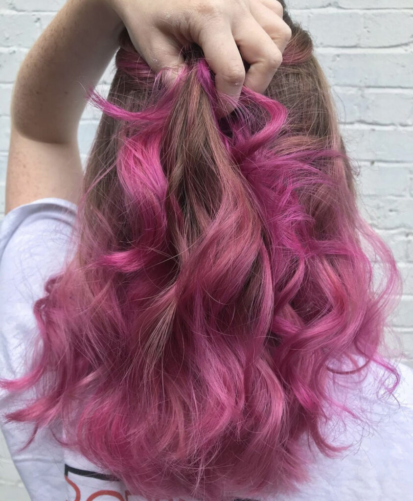 back of womans head. woman is holding a section of hair which is coloured pink