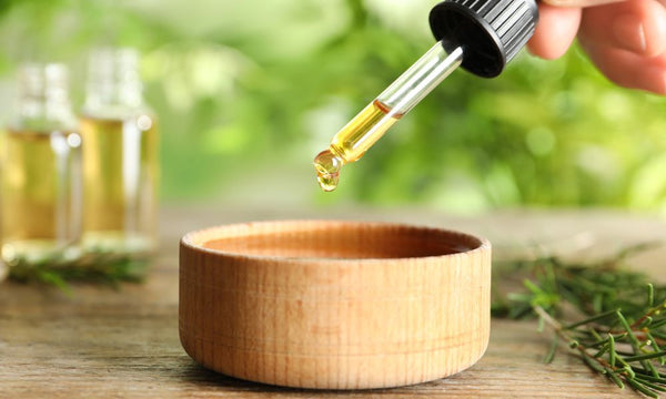 wooden bowl with someone using a dropper to measure essential oils for mixing